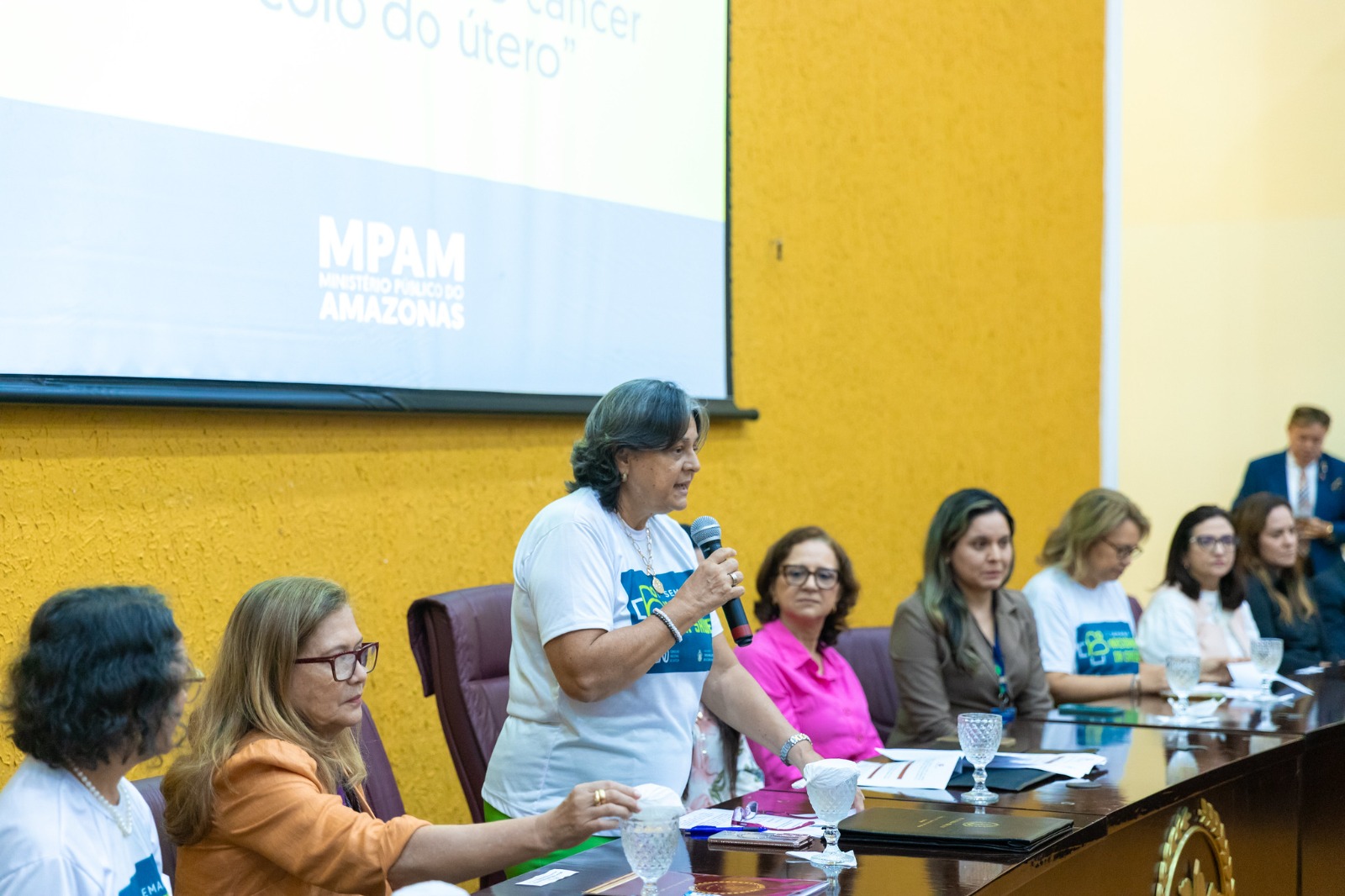 Foto mostra a desembargadora Luiza Cristina falando ao público durante evento: ele aparece ladeada por autoridades